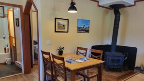 Un salon chaleureux avec une table à manger en bois, quatre chaises, un poêle à bois noir et deux tableaux encadrés accrochés au mur.
