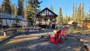 Un chalet doté d’une terrasse en bois, de chaises Adirondack rouges et d’une cheminée en pierre.