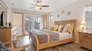 Une chambre avec un lit en bois, un ventilateur de plafond, un bureau et une chaise.