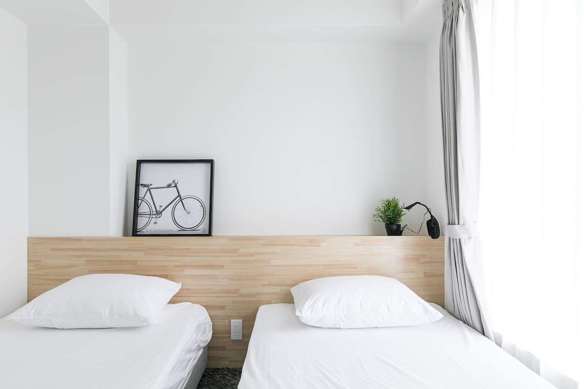 A hotel room with two beds, a wooden headboard, a framed bicycle artwork, a small potted plant, and a window with curtains.