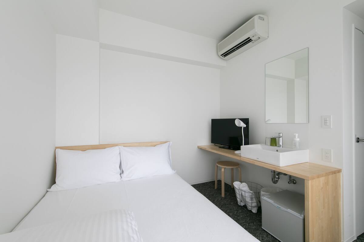 A hotel room with a bed, a desk with a computer, a mirror, and a small stool.