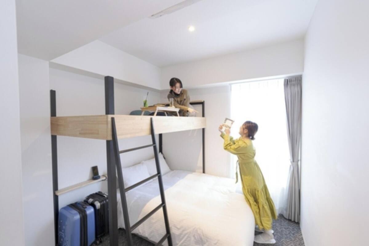 A bunk bed room with a ladder, a desk, and a suitcase.