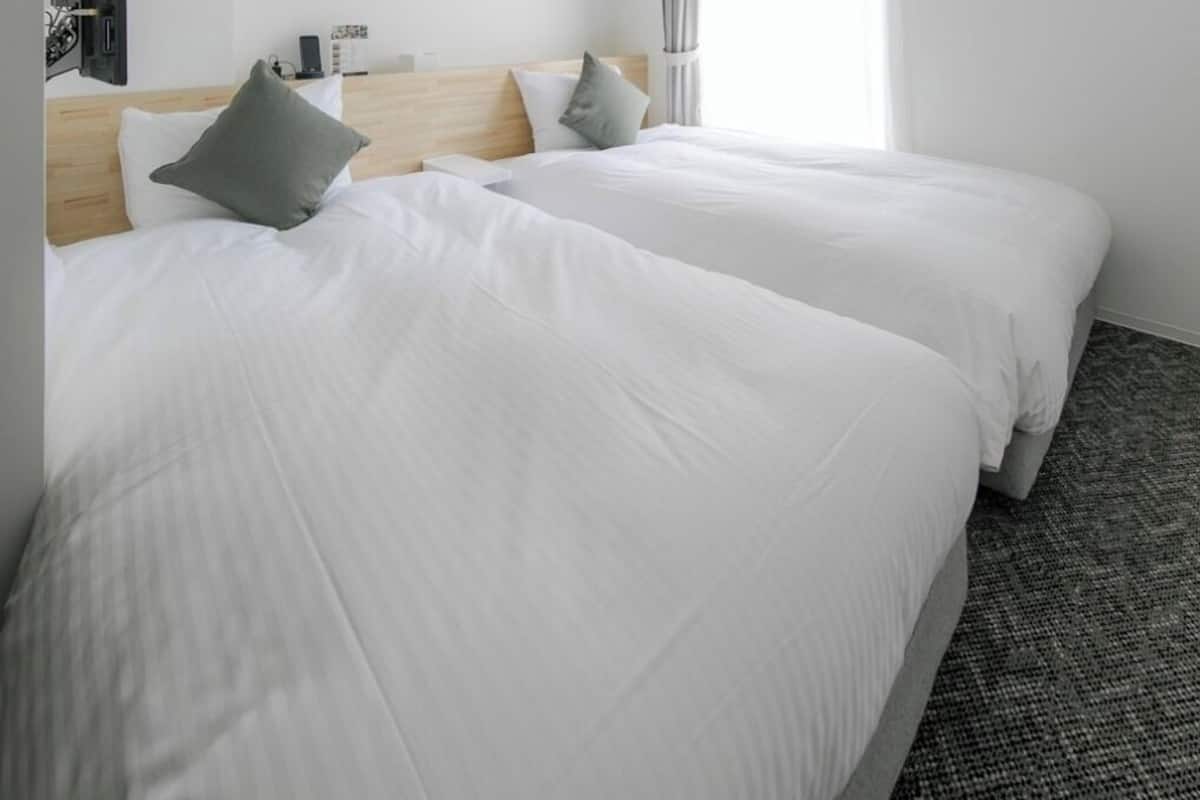 A hotel room with two beds, a flat-screen TV, a desk, and a window with curtains.