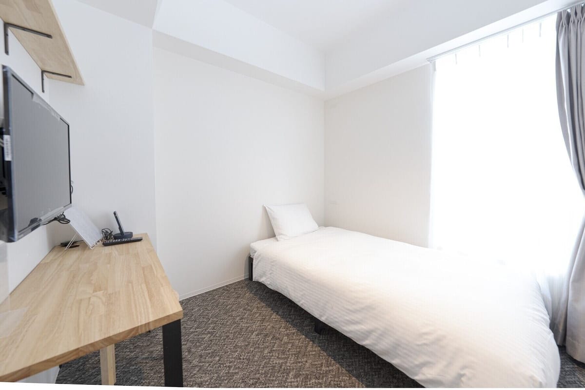 A hotel room with a bed, a desk with a computer, and a TV.