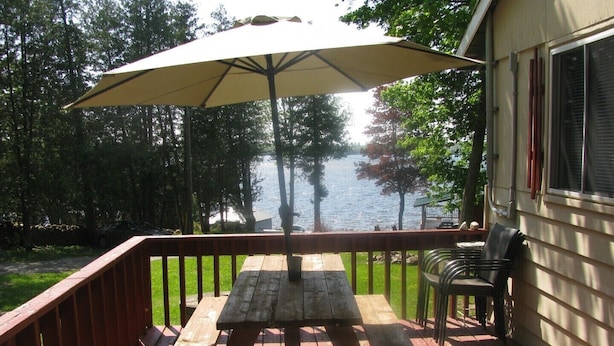 Une terrasse en bois avec une table de pique-nique et un parasol, d’où l’on a vue sur une étendue d’eau et des arbres.