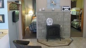 Une pièce avec une cheminée en pierre, une radio, un téléviseur et, au fond, un lit superposé.
