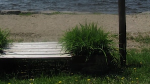 Un panneau indicateur en bois portant l’inscription « Plage privée du centre chrétien de Shiloh », une jetée en bois et une plage de sable avec de l’herbe et des fleurs sauvages.