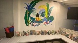 A room with a long white bench, colorful pillows, and a wall mural with tropical designs. - Plantation House (Hikkaduwa)