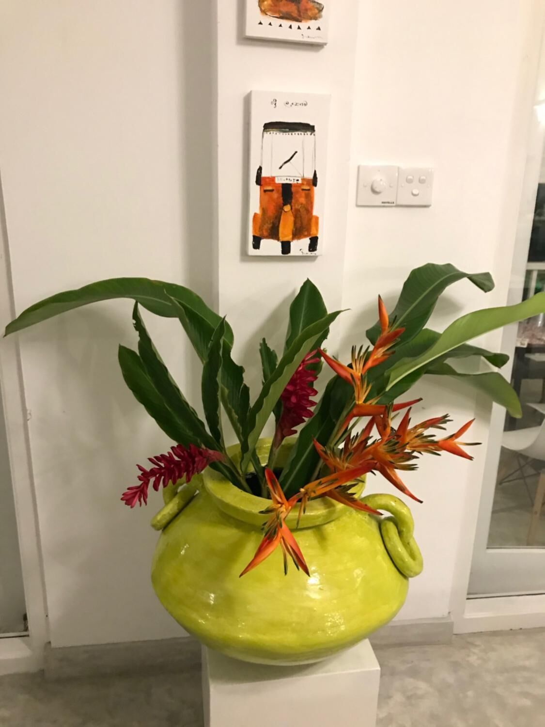 A green vase with a plant on a white pedestal against a white wall.