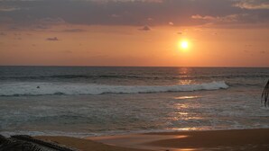 A beach with the sun setting over the ocean, waves gently crashing onto the shore. - Plantation House (Hikkaduwa)