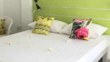 Una cama con ropa de cama blanca y almohadas decorativas, una lámpara de noche y un cabecero verde.