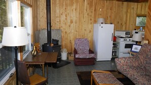 Ein gemütliches Blockhaus-Interieur mit Holzausstattung, einem Esstisch mit Stühlen, einer Couch, einem Kühlschrank, einem Herd und einem Fenster, das für natürliches Licht sorgt.