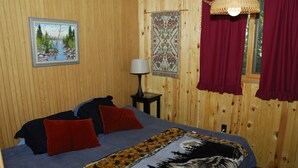 Ein Zimmer mit Holzwänden, einem Bett, Kissen, einer Lampe, einem Teppich und einem Bild an der Wand.