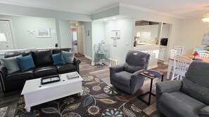 A living room with a black leather sofa, a grey armchair, a white coffee table, and a patterned rug. - Fall is beautiful,beach locker & chairs/ 8 min walk to Shipyard Beach (Hilton Head Island)