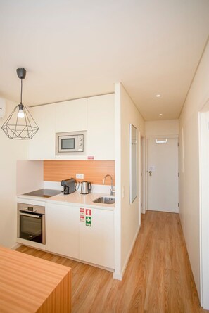 Cocina compacta con microondas, estufa y pileta. Hay una mesa de madera y una lámpara colgante.