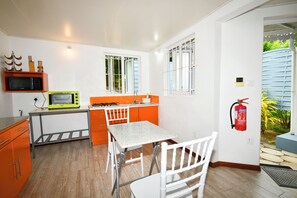 A compact kitchen with a microwave, a gas stove, and a sink. There is a white table and chairs, and a fire extinguisher mounted on the wall.
