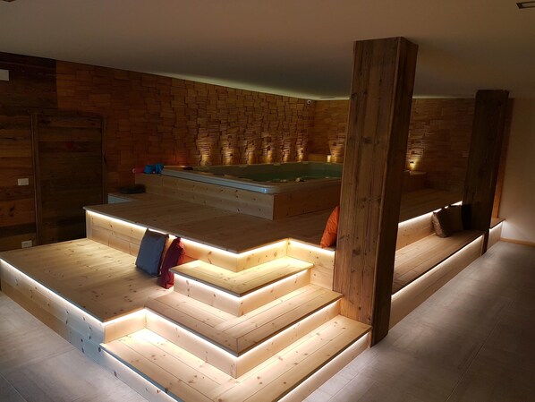 A modern bathroom with wooden walls, a built-in bathtub, and a wooden bench with steps leading to the tub.