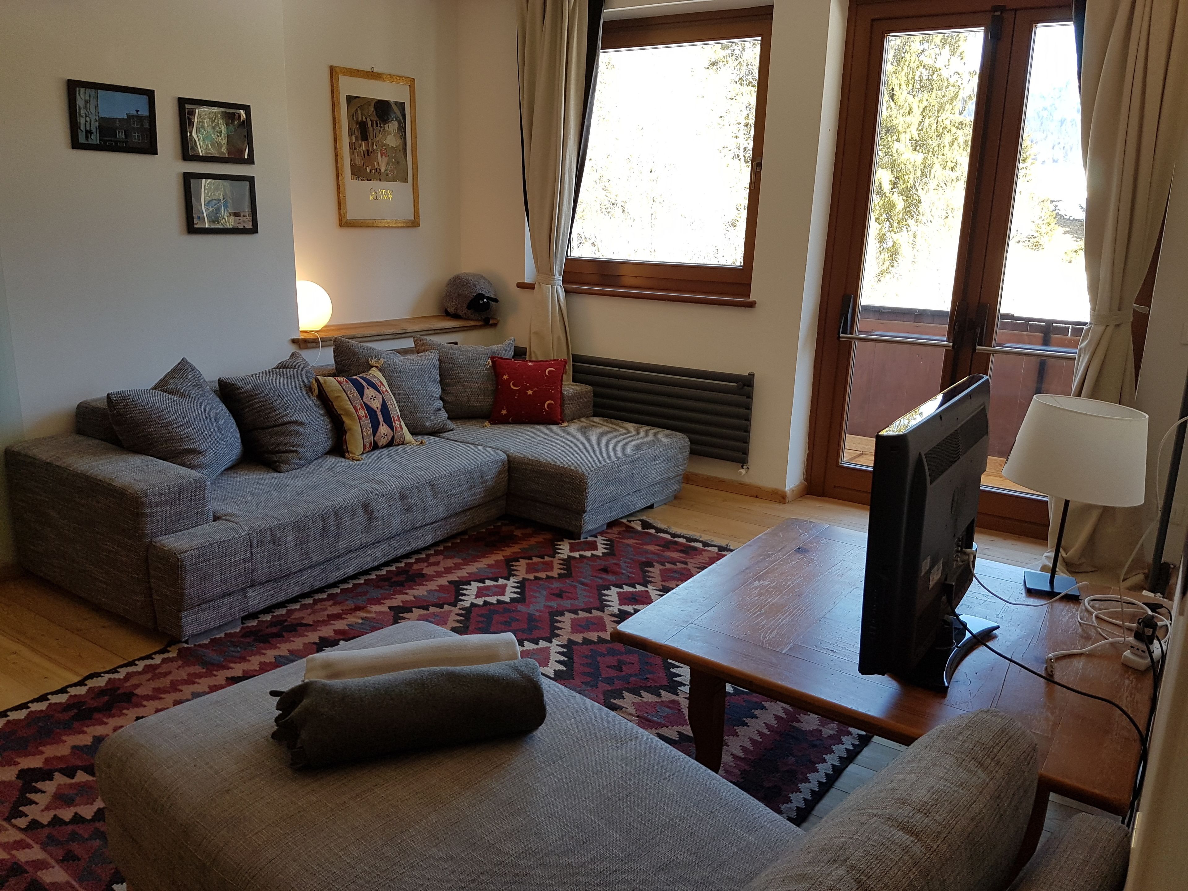 A living room with a sectional sofa, a flat-screen TV, a small table, and a patterned rug.