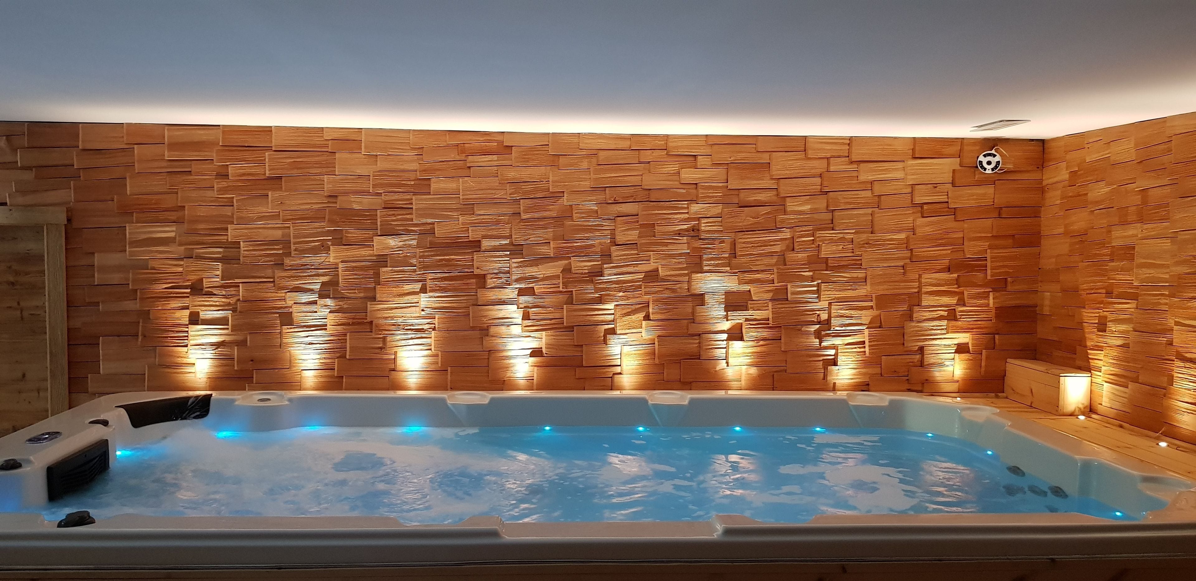 Vasca idromassaggio con parete a muro in legno e plafoniera.
