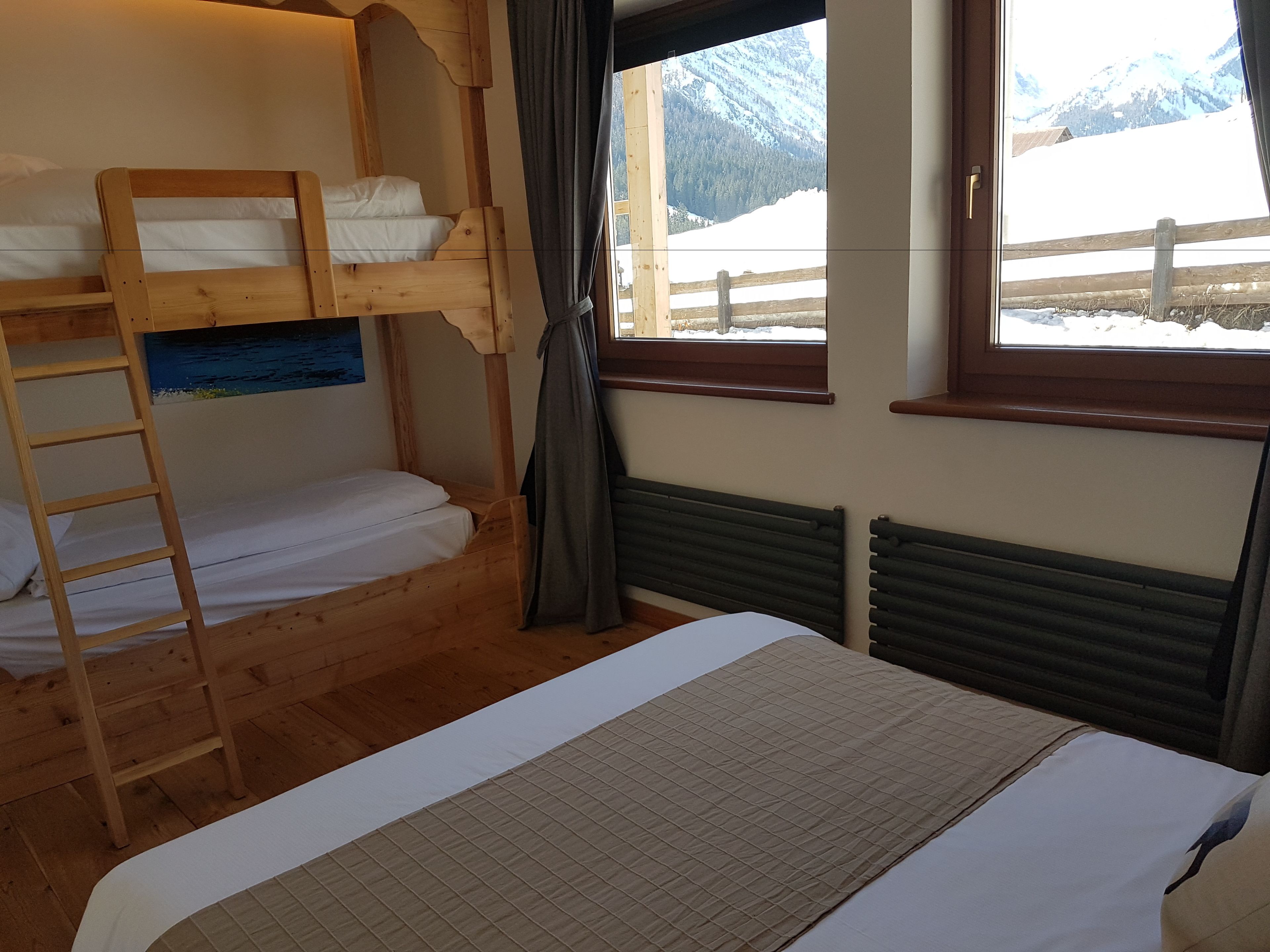 A room with bunk beds, a wooden ladder, a window with a view of snow-covered mountains, and a radiator.