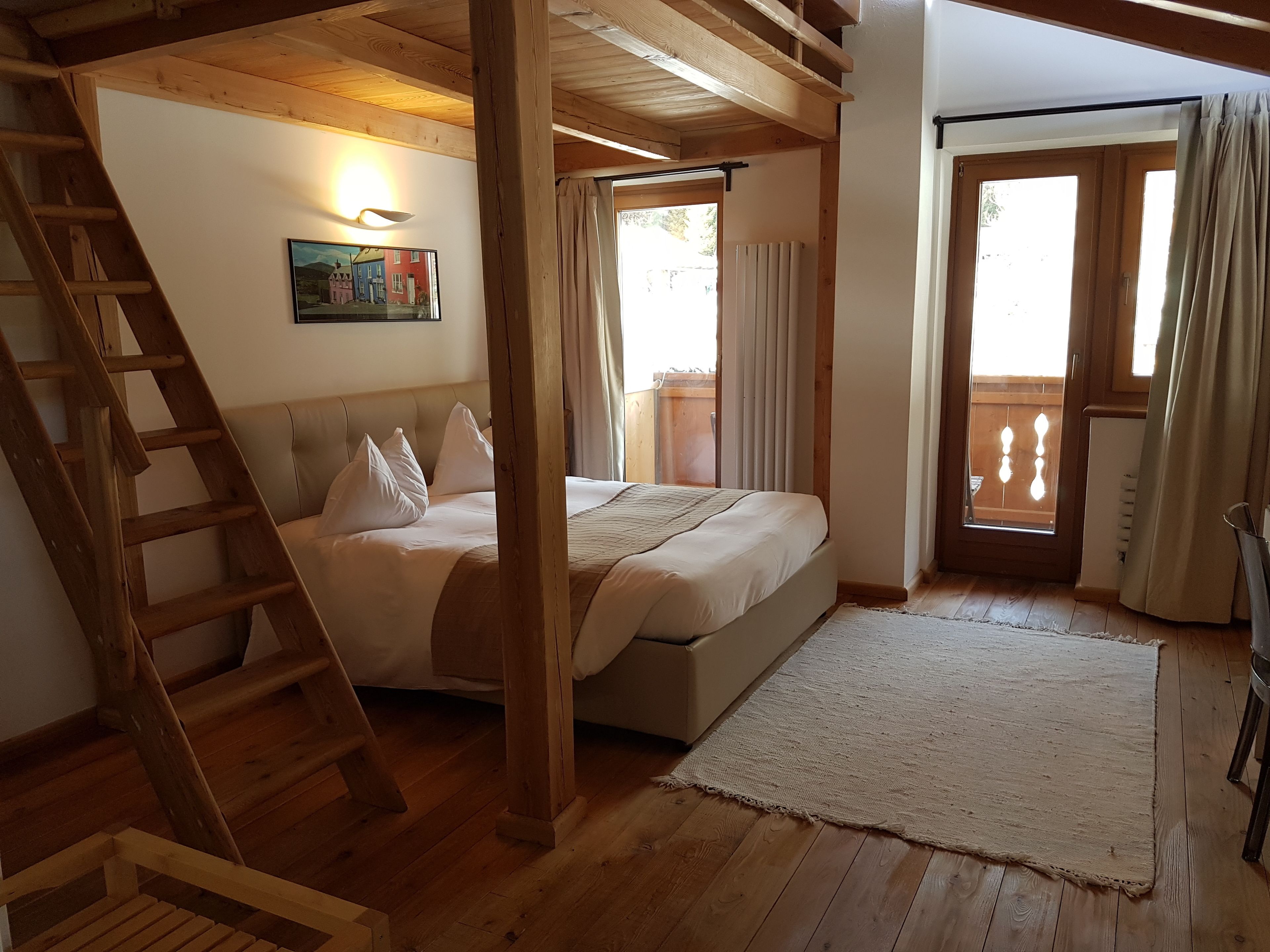 Quarto com escada de madeira, cama com roupa de cama branca, quadro na parede e vista pela janela.