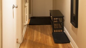 Een gang met houten vloer, een witte deur, een zwarte bank en een spiegel met zwart frame aan de muur.
