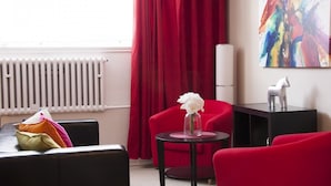 Een moderne kamer met een rode stoel, een zwarte bank en een kleine tafel met een witte bloem.