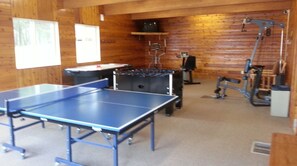 Een kamer met een tafeltennistafel, fitnessapparatuur en een klein tafeltje met een stoel.