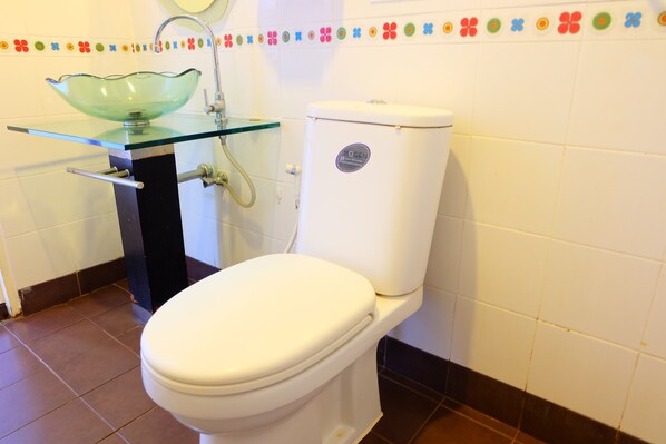Un baño con un lavabo de cristal, un inodoro blanco y un borde de azulejos decorativos.