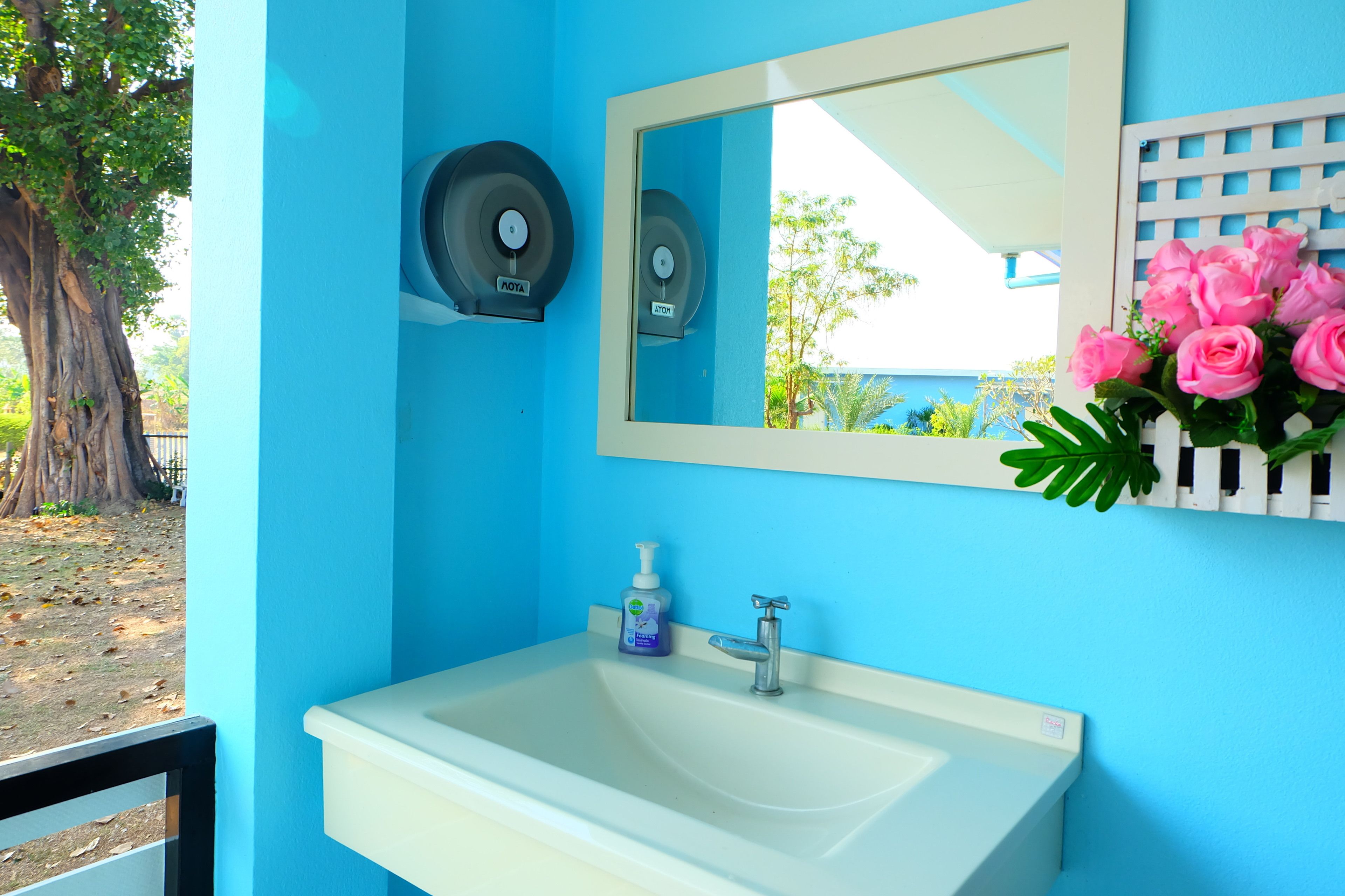 Casa de banho com parede azul, pia branca, espelho e arranjo floral rosa.