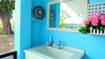 Casa de banho com parede azul, pia branca, espelho e arranjo floral rosa.