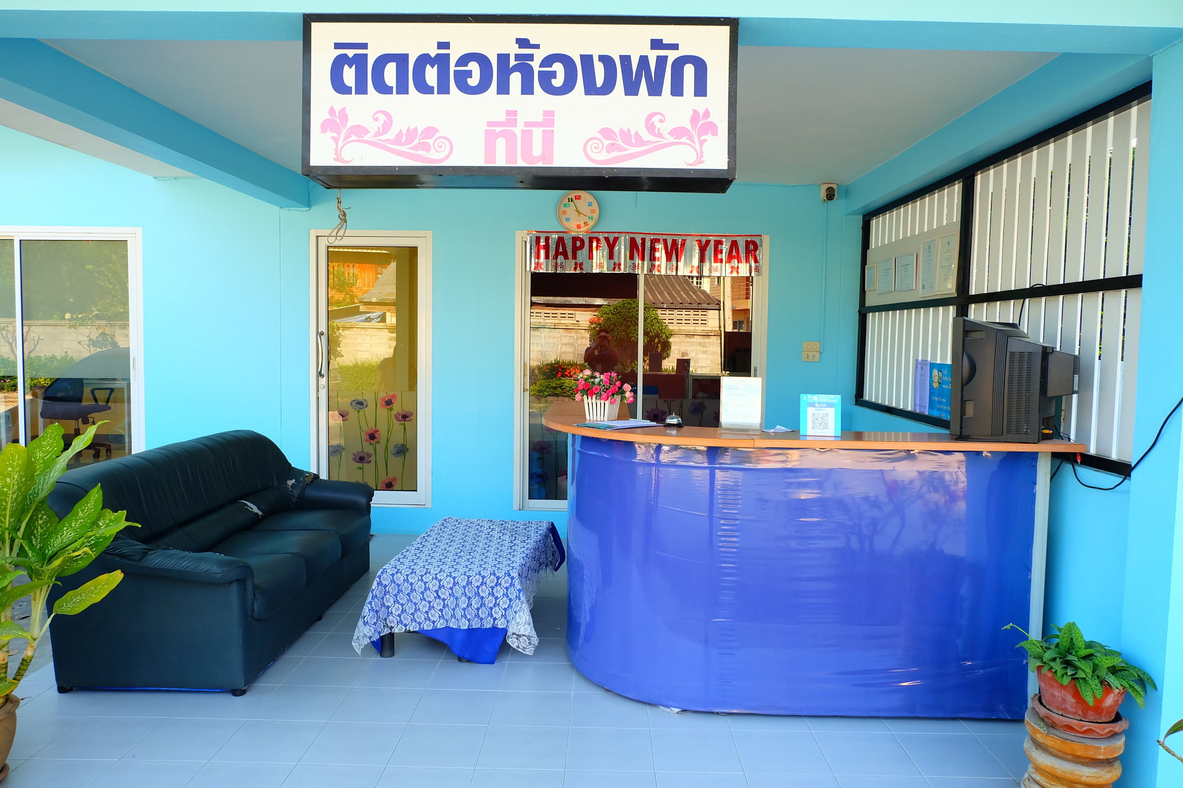 Una zona de recepción con una pared azul, un sofá de cuero negro, una mesita con mantel estampado y un cartel que dice 'Happy New Year'.