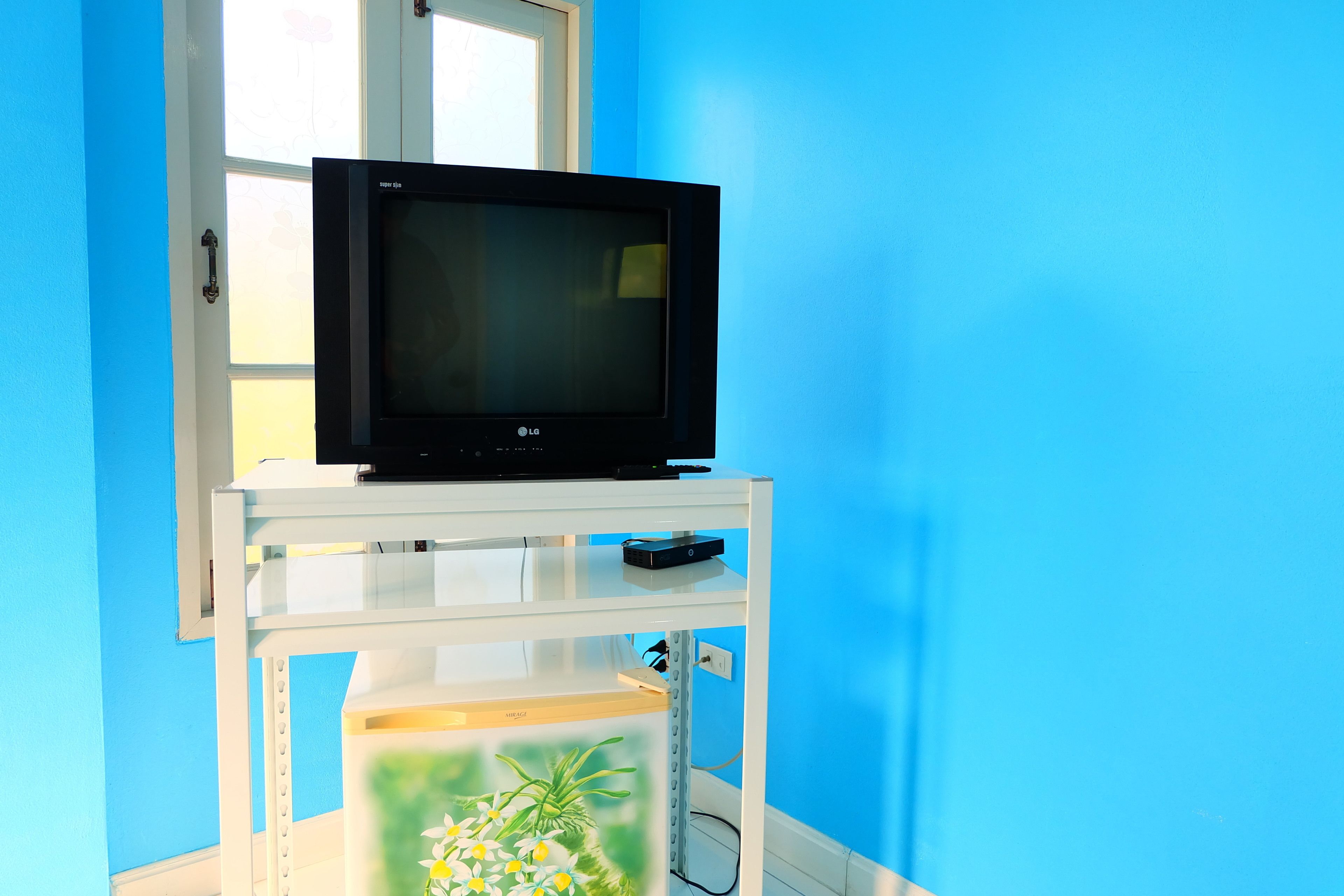 A television on a white stand with a window behind it.
