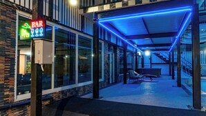 Eine Bar mit einer Neonreklame, Außenbereich und einem überdachten Bereich mit blauer Beleuchtung.
