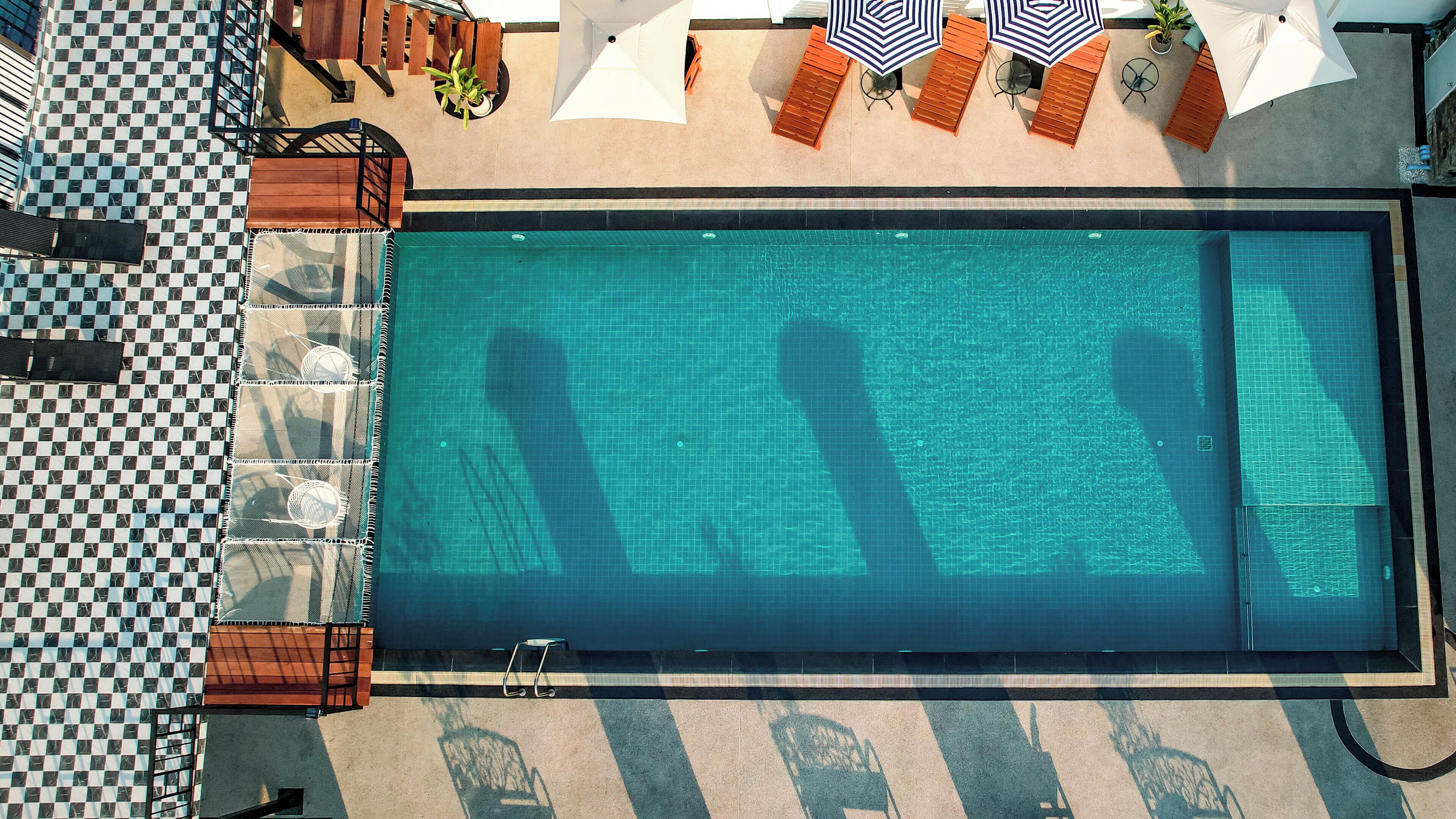 Una gran piscina rectangular con un estampado de ajedrez alrededor, acompañada de sillas de descanso y sombrillas.