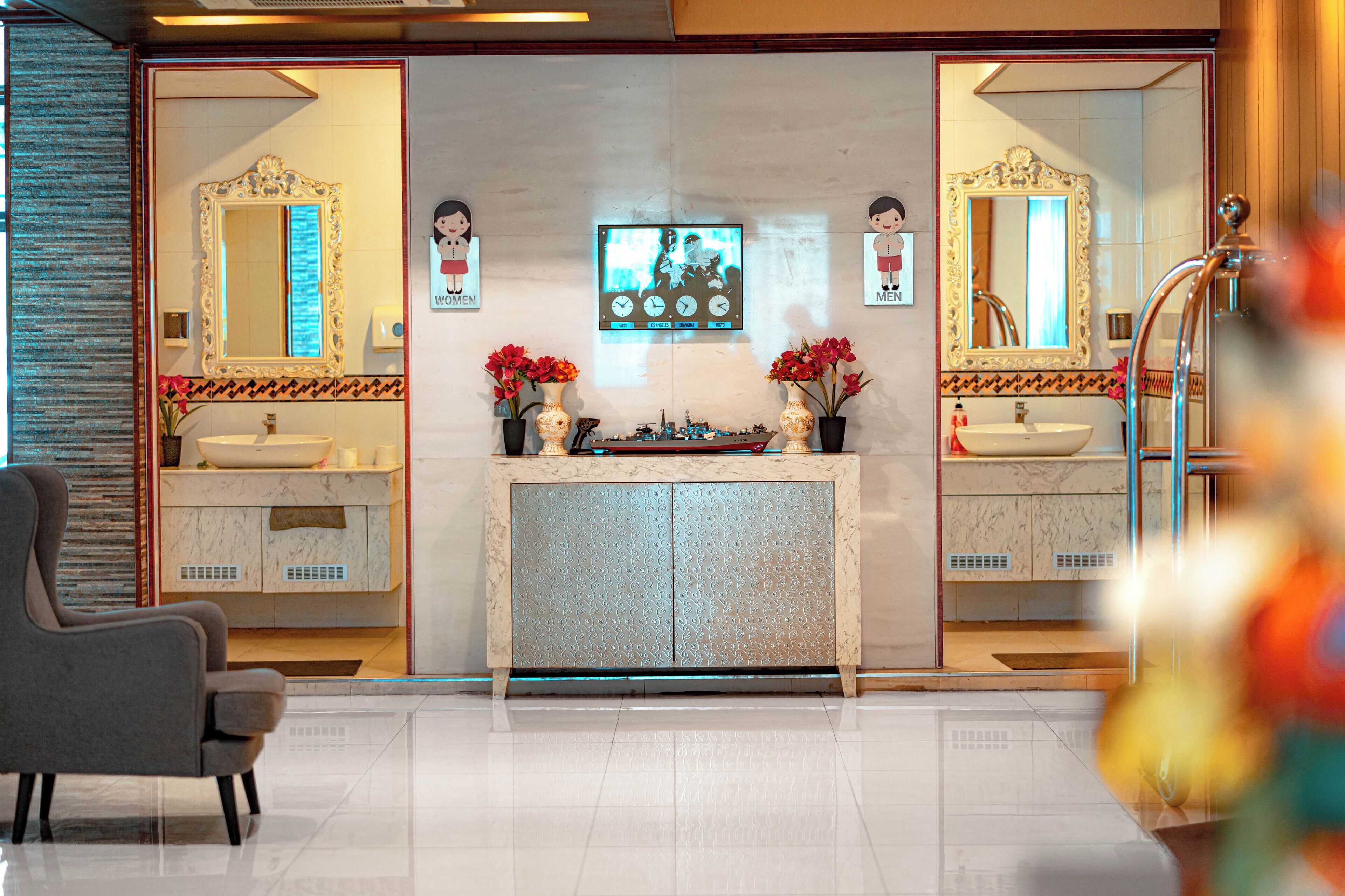 A modern bathroom with two sinks, a vanity, and a large mirror. There are decorative flowers on the vanity and a clock on the wall.