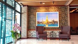 Eine Lobby mit zwei Sesseln, einem großen gerahmten Bild eines Tempels und einem Orchideenstrauch.