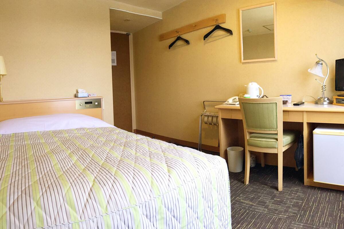 Una habitación de hotel con cama, escritorio, silla y un refrigerador pequeño.