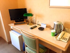 Scrivania in camera d'albergo con televisore, lampada, telecomando, tazza da caffè, bollitore e telefono.