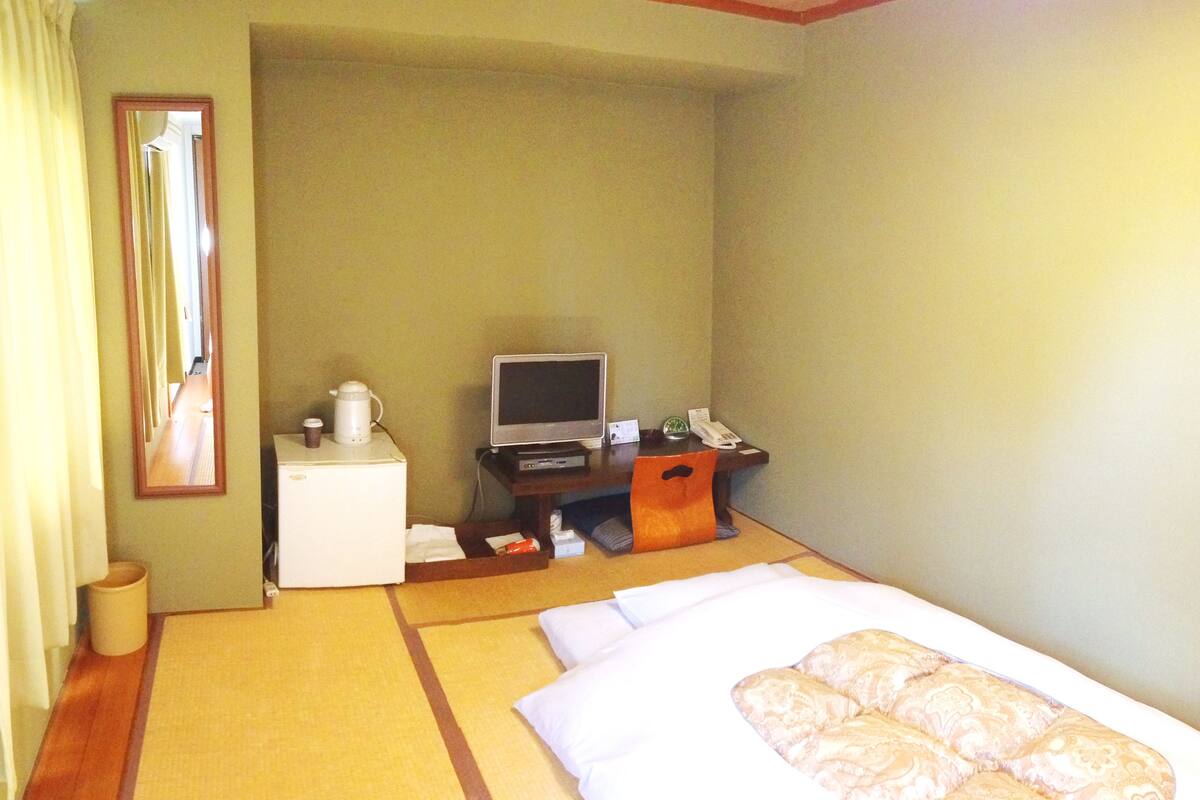 Habitación de hotel con cama, escritorio, computadora, teléfono y un refrigerador pequeño.