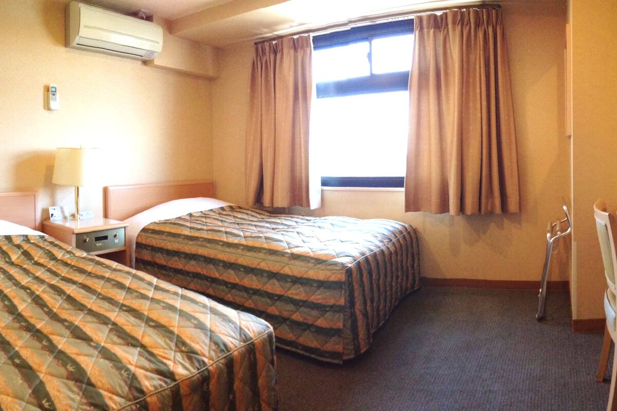 Habitación de hotel con dos camas, un escritorio, televisor, lámpara y aire acondicionado.