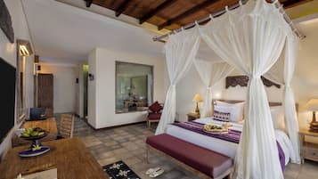 A bedroom with a four-poster bed, a dining area with a table and chairs, and a view of the room through a window.