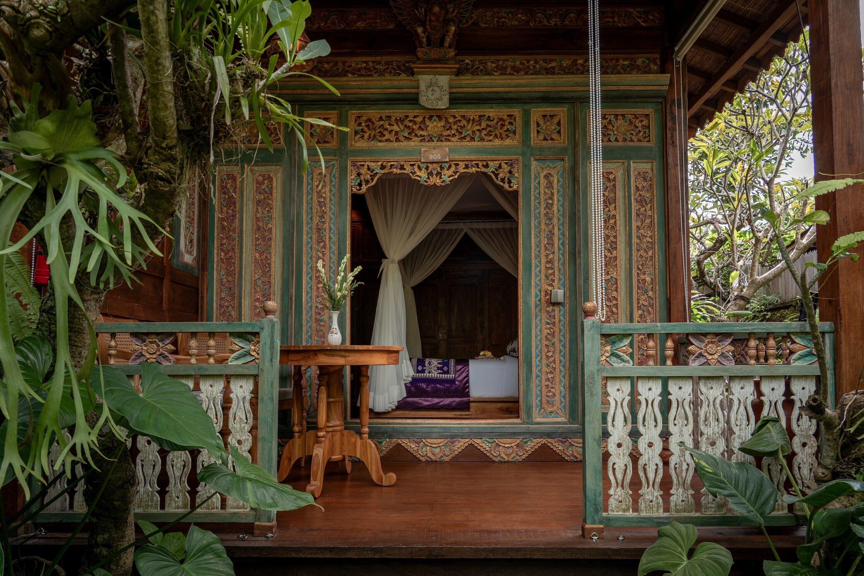 A traditional wooden structure with intricate carvings, a small table, and a bench with a purple cushion.