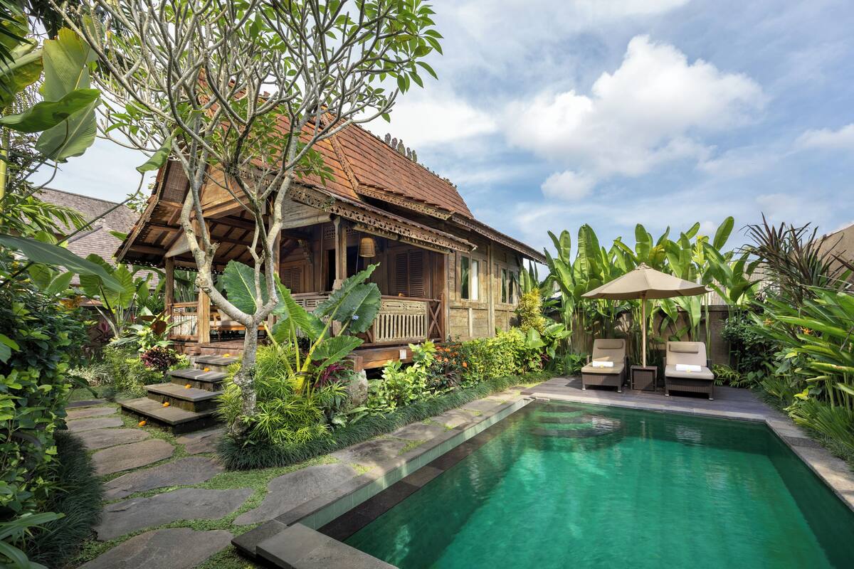 A traditional wooden house with a tiled roof, a swimming pool, and lounge chairs.