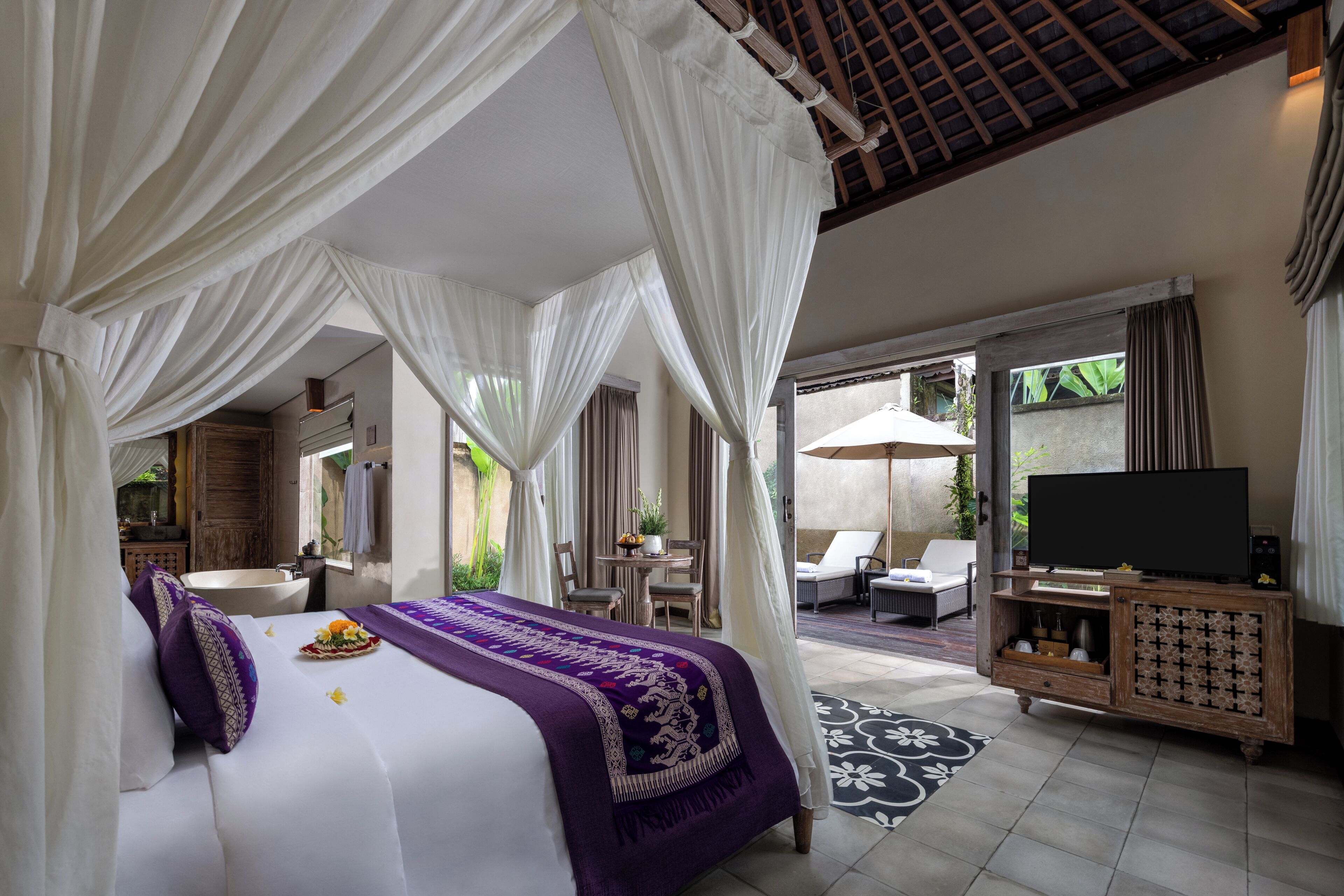 A bedroom with a bed, a TV, a bathroom, and a seating area with a view of the outdoors.