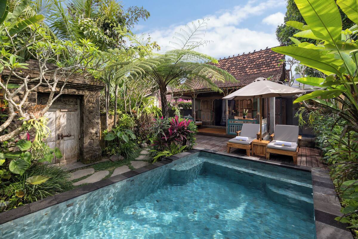 A swimming pool with lounge chairs and a covered seating area surrounded by lush greenery.