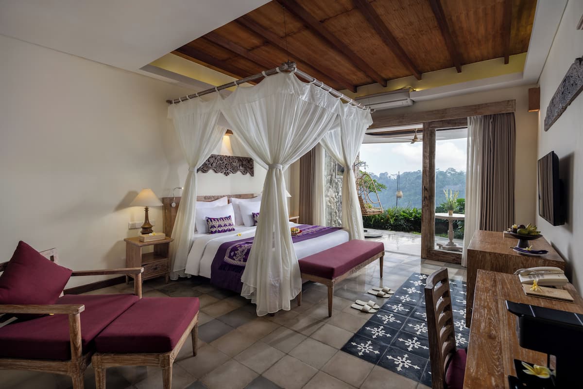 A bedroom with a canopy bed, a desk, and a view of the outdoors.