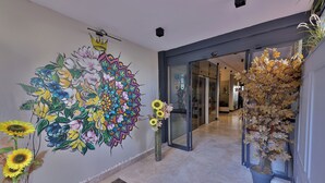 A hallway with a large floral mural, a potted plant, and a glass door leading to another room. - BUCA MAT HOTEL BY TAHTALI (Izmir)