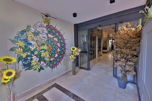 Un pasillo con un gran mural floral, una planta en maceta y una puerta de cristal que da a otra habitación.