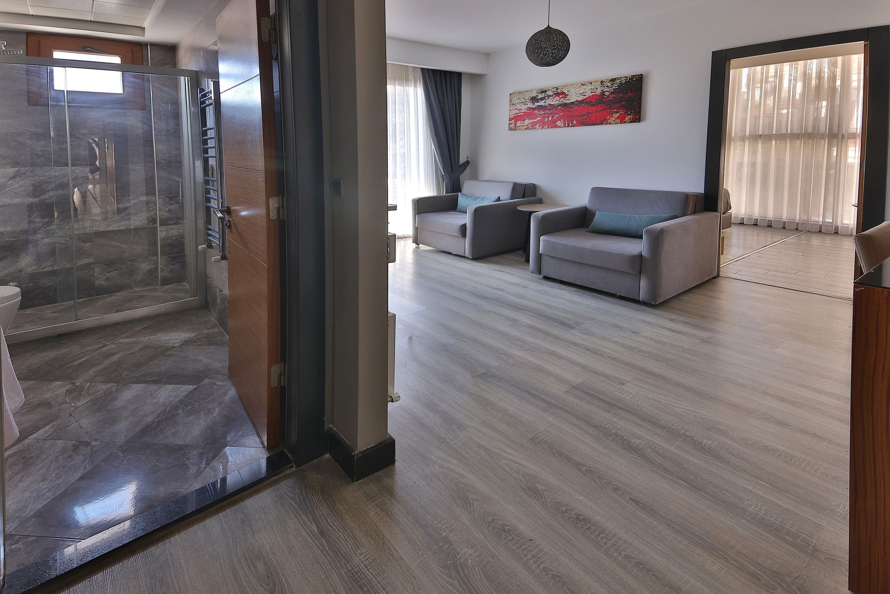 A modern living room with a glass shower enclosure, a grey sofa set, and a large abstract painting on the wall.